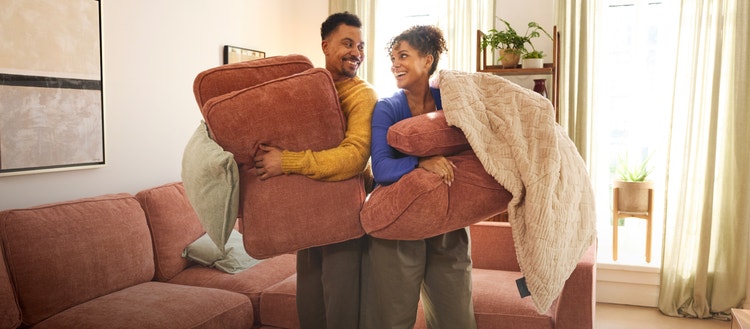 Two people rearranging their orange, Lovesac, sectionals couch in their living room