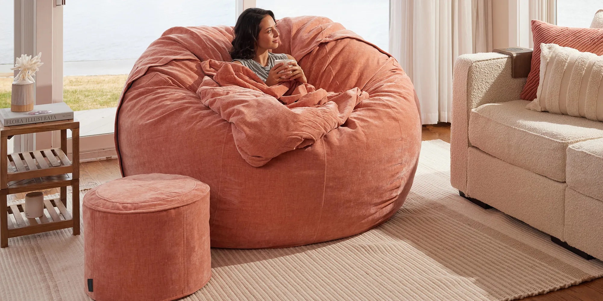 Woman relaxing on a Lovesac Sac bean bag chair with blanket and Squattoman footstool