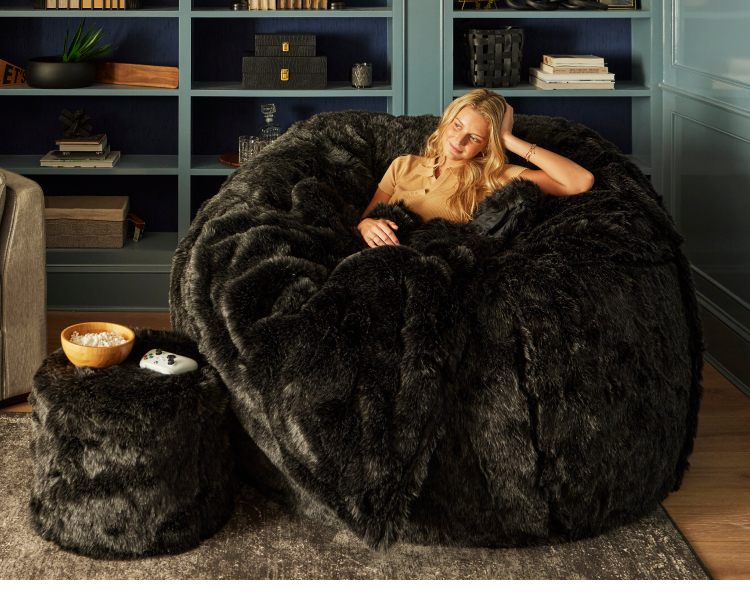 Woman relaxing on a Lovesac Sac bean bag chair with blanket and Squattoman footstool
