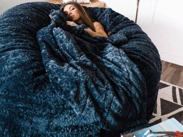 Girl napping on a Lovesac SuperSac bean bag chair with a blanket.