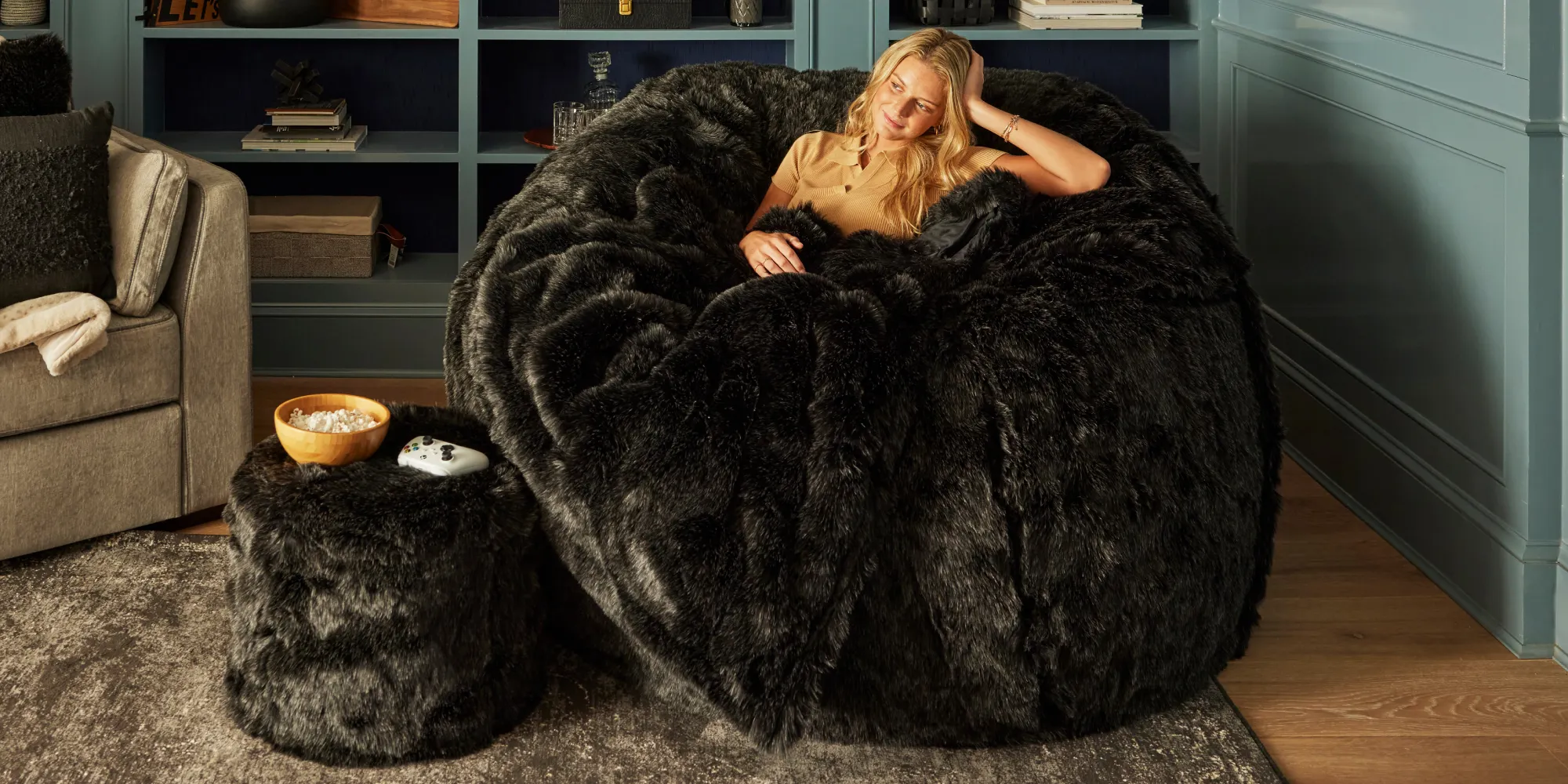 Woman relaxing on a Lovesac Sac bean bag chair with blanket and Squattoman footstool