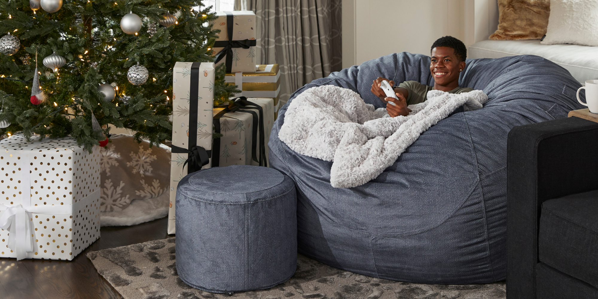Teenager playing a video game while sitting on a Lovesac Sac large bean bag chair with a blanket