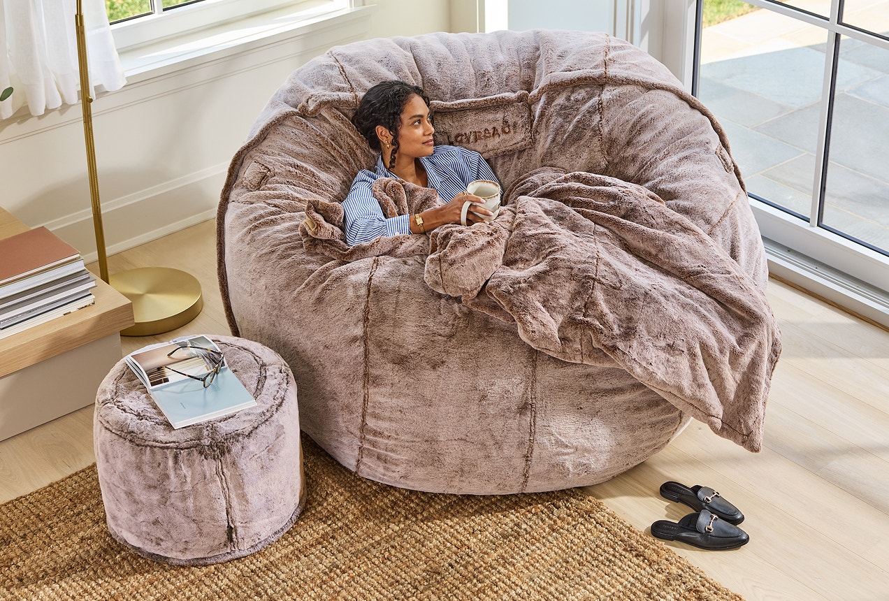 Woman relaxing on her Lovesac PillowSac Accent Chair with matching ottoman