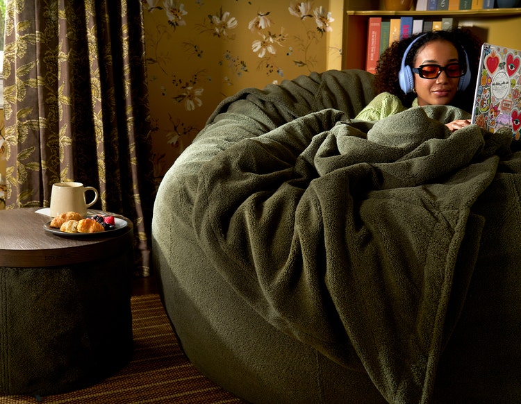 Woman relaxing on a grey colored Lovesac bean bag chair with her dog.