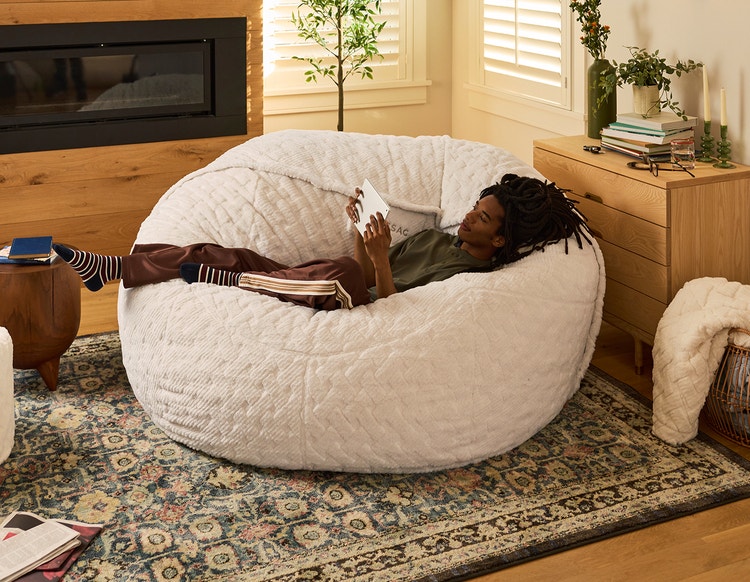 Woman relaxing on a grey colored Lovesac bean bag chair with her dog.