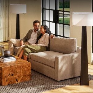 A man and woman relaxing on a taupe, 2-cushion sofa in a living space