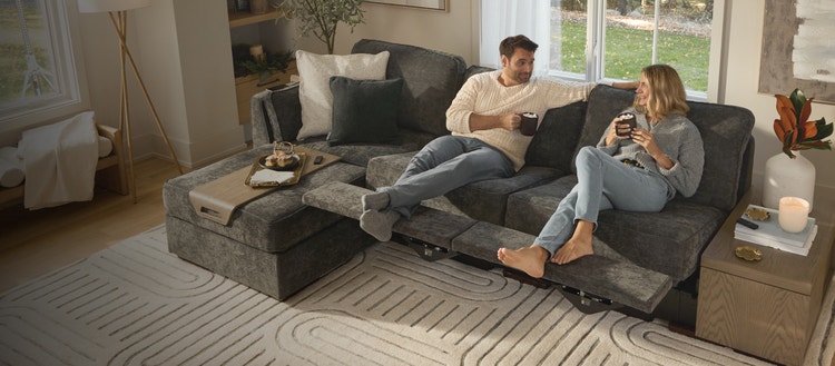 Couple relaxing on their grey Lovesac sectional couch with reclining seats.