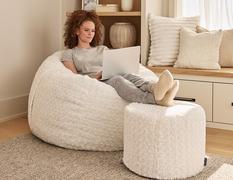 Woman sitting on a Lovesac beanbag chair with matching ottoman