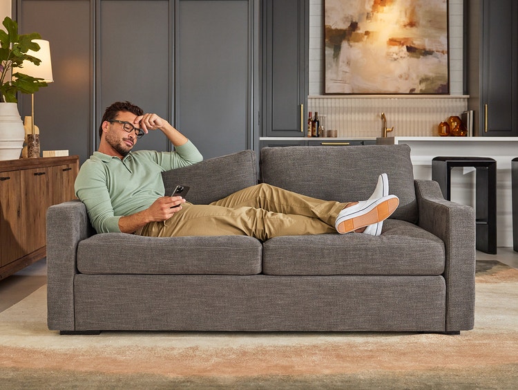 Man relaxing on a grey loveseat with swept arms in a living space