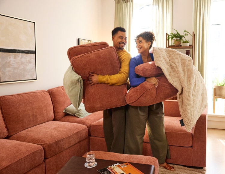 Two people rearranging their orange, sectional sofa
