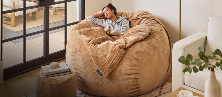 Woman relaxing in caramel colored Lovesac beanbag chair in a living room