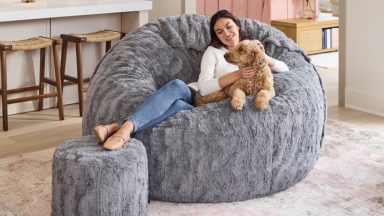 Woman and dog relaxing in a large grey Lovesac beanbag chair and ottoman.